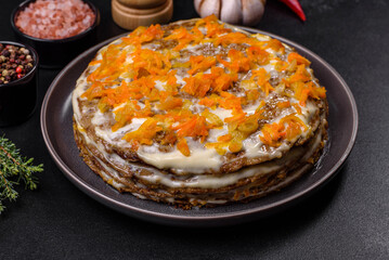 Delicious fresh liver cake with mayonnaise and carrots on a black plate against a dark concrete background