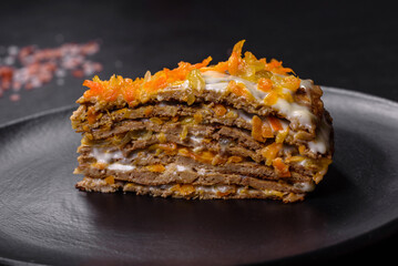 Delicious fresh liver cake with mayonnaise and carrots on a black plate against a dark concrete background