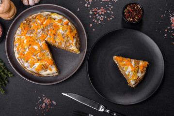 Delicious fresh liver cake with mayonnaise and carrots on a black plate against a dark concrete background