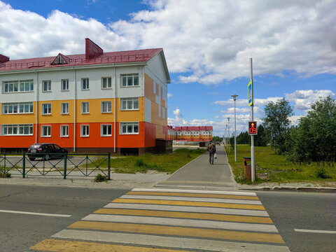 Noyabrsk, Russia - July 7, 2022: View of bright three-story houses with a parking area in a new microdistrict of the city. People walk along the sidewalk along the houses