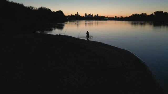 A lone fisherman on the banks of the Vistula River in the glow of the setting sun over the skyscrapers of Warsaw