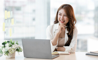 Image of smiling beautiful woman thinking and looking outside while sitting at table in office.
