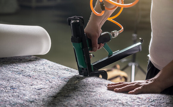 An employee holds in his hands an industrial air stapler for sheathe soft fabric upholstery. Close-up