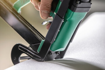 An employee holds in his hands an industrial air stapler for sheathe soft fabric upholstery....