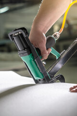 An employee holds in his hands an industrial air stapler for sheathe soft fabric upholstery. Close-up