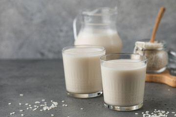 Glasses of vegetable rice milk and a jug on a gray background. Vegetarian food, lactose free milk. Copy space