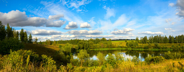 Summer panoramic landscape with pond and green trees at sunset