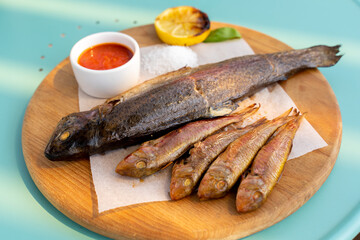 Large and small fried fish on a wooden board, Sauce, salt. close-up.