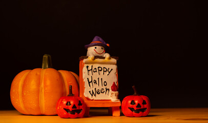 Halloween pumpkins with painted faces and ghost dolls on old wood desk, black background and copy space for text