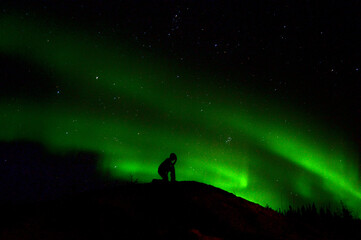 Naklejka na ściany i meble silhouette of a person in the night with aurora borealis background northern lights