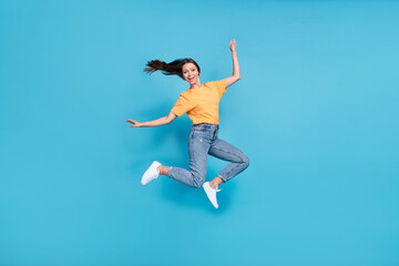 Fototapeta na wymiar Full length photo of excited pretty girl dressed yellow t-shirt finger rising arms hands jumping high isolated blue color background