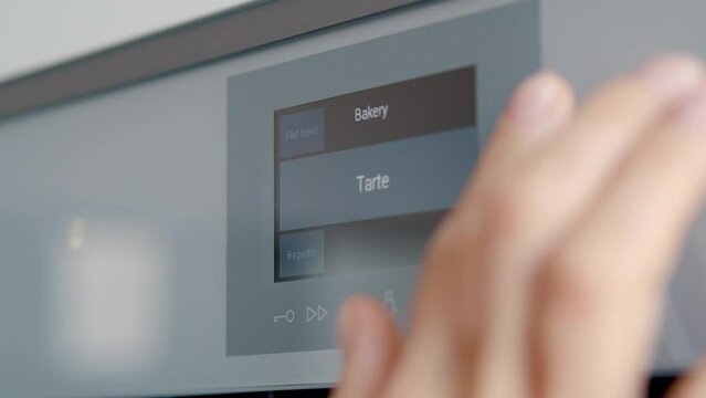 Close up of woman hand choose program on electronic control panel for built-in oven in kitchen. 