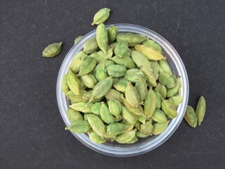 Green cardamom in a glass bowl on black background top view 