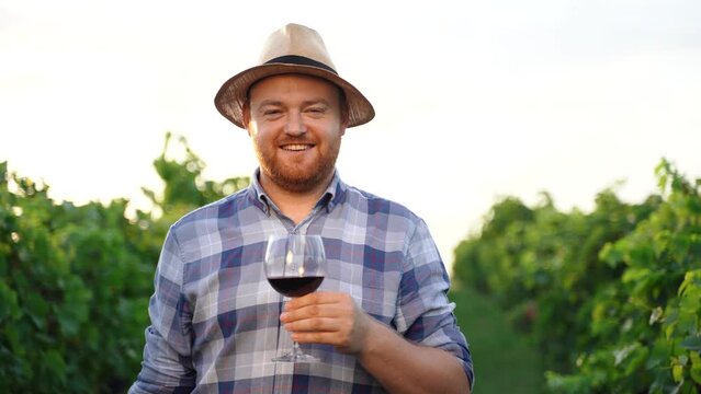 Young positive sommelier mixing red wine in glass evaluating color at tasting. Private wine tasting tour in summer. Winemaking concept.