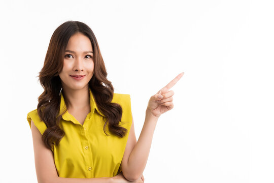 Hey look. Smiling pretty Asian woman pointing fingers left at empty space and inviting to check it out, showing advertisement on white background.