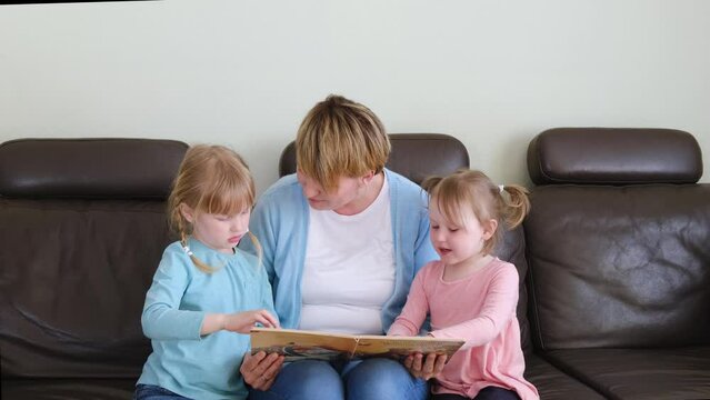Mother and preschool cute daughters having fun at home, eading fascinating fairy tale book.