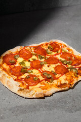 Traditional italian food - Pizza pepperoni on dark background. Pepperoni pinsa on gray stone table with hard shadow. Roman pizza with pepperoni and jalapeno on concrete background. Pinsa menu.