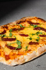 Italian pizza with cheese and dried tomatoes on dark background. Cheese pinsa on gray stone table with hard shadow. Roman pizza with cheese and tomatoes on concrete background. Pinsa menu.