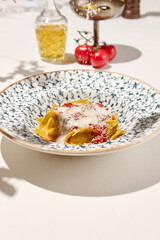 Italian ravioli with spinach, cheese and tomato in ceramic plate on white table. Cheese ravioli with creamy espuma and tomato. Italian ravioli with spinach and cheese filled and creamy topped.