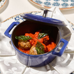Traditional italian meatballs in tomato sauce on white table. Beef meatballs in ceramic pot in italian style with tomato and basil. Main course from meat in elegant style. Homemade meatballs.