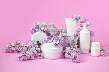 Fototapeta na wymiar Face and body skin care. A set of cosmetic creams and balms in white tubes and cans on a coral background with sprigs of lilac flowers. Spa treatments for home care. Home rejuvenation and moisturizing