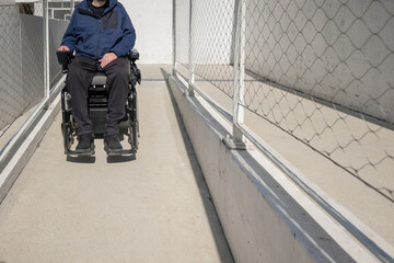 Man on electric wheelchair moving along concrete accessibility pathway near the building. Concept...