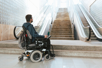 Man with disability on wheelchair stopped in front of staircase, raising awareness of architectural...
