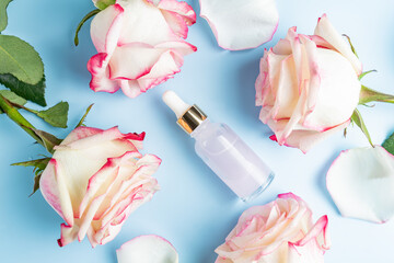 Cosmetic serum with essential rose oil and roses on a blue background. A natural product for...
