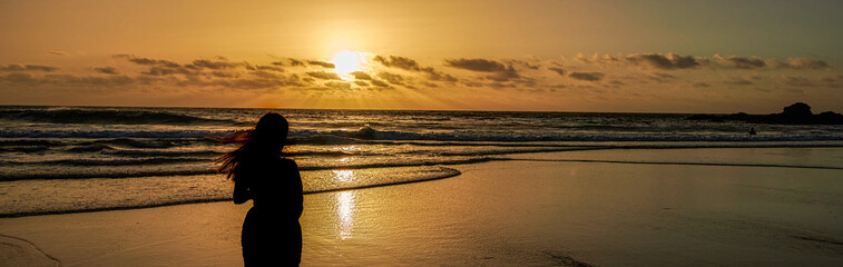 Silhouette of a young woman watching the sunset on the beach,