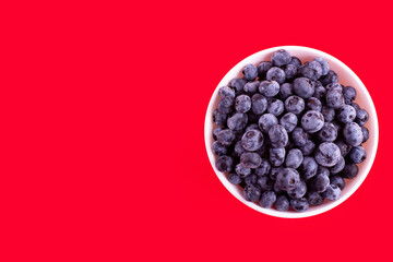 Top view of fresh juicy ripe blueberries in bowl isolated on red. Flat lay copy space. Healthy berry, organic food, antioxidant, vitamin, blue food.