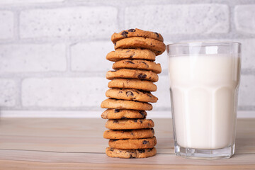 Composition of freshly baked homemade biscuits with chocolate chips. Healthy breakfast concept with glass of milk and cooked cookies on wooden table for overlay on product presentation..
