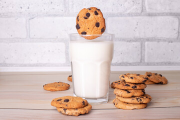  The chocolate chip cookie biscuit levitates in the air over a glass of milk on wooden table, on the kitchen. Sweet food concept. Flatlay an after school snack of chocolate chip cookies.