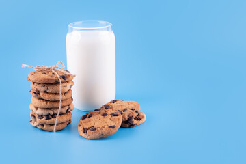 Glass of fresh milk and brown school chocolate cookies on blue background. Sweet food yummy and tasty concept. Flatlay an after school snack of chocolate chip cookies.