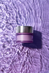 Purple cosmetic jar on the purple water surface. Blank label for branding mock-up. Summer water...