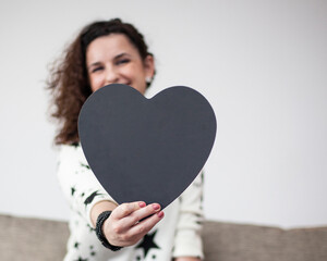Smiling woman holding a wooden board in the shape of a heart that you can write on with chalk