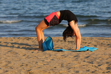 young slender girl does gymnastic exercises at the beach on the gym mat
