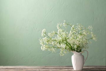 white wild flowers in jug on background green wall