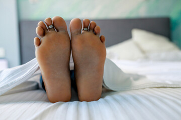 Close up of female feet in bed in bedroom under blanket