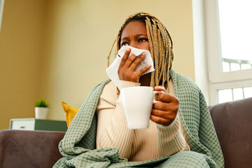 afro american woman covered with blanket blowing running nose holding tea cup