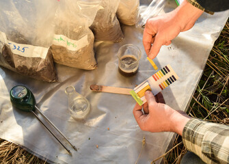 Male agronomy specialist testing soil sample outdoors, using laboratory equipment, performing soil...