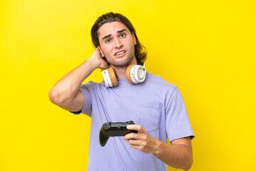 Young handsome caucasian man playing with a video game controller over isolated on yellow background having doubts