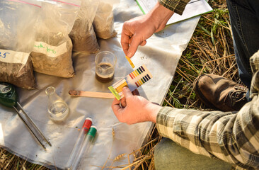 Male agronomy specialist testing soil sample outdoors, using laboratory equipment, performing soil certification at agricultural grain field sunrise. Environment research, soil certification