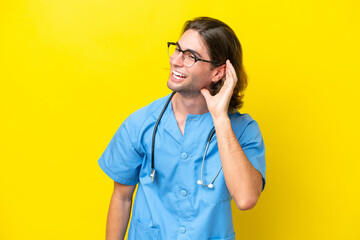 Young surgeon caucasian man isolated on yellow background listening to something by putting hand on the ear