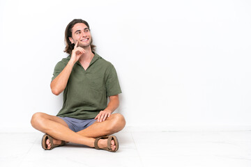 Young handsome man sitting on the floor isolated on white background thinking an idea while looking up