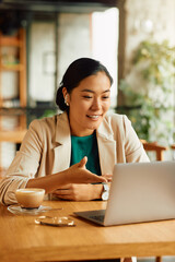 Happy Asian businesswoman having video call over laptop in cafe.