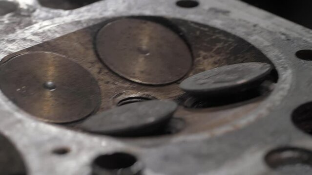 An old valve head contaminated with soot and rust. Close-up, the camera travels parallel to the valves. Dark background.