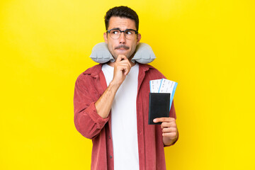 Young handsome man with Inflatable Travel Pillow over isolated yellow background having doubts and...