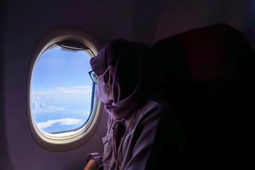A female passenger is looking at the view of the blue sky from the cabin of the plane.