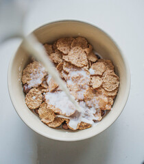 pouring milk into a white bowl with corn flakes, top view