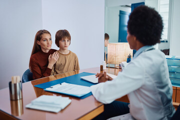 Smiling mother and son talk to black female pediatrician at doctor's office.